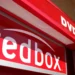 Close-up view of a redbox DVD rental kiosk. The bold red cabinet has the word "redbox" prominently displayed in white text, along with "DVD RENTALS" above it. The kiosk is situated outdoors against a beige wall, with some daylight visible—an everyday sight for investors keeping an eye on RDBX stock. | 5StarsStocks