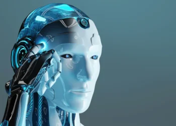 A futuristic humanoid robot with a sleek white and metallic blue design holds its hand to the side of its head. The 5StarsStocks AI robot features illuminated blue accents and a transparent dome revealing electronic components. The background is a gradient of blue shades. | 5StarsStocks