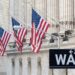 Four American flags fly in front of buildings with columns on Wall Street. A black street sign displaying "Wall St" with arrows pointing to 22-51 is in the foreground. The stone buildings are well-lit with natural light, embodying the financial essence of Wall Street, home of the Dow Jones. | 5StarsStocks