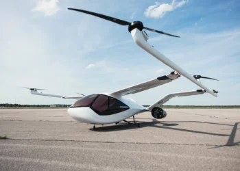 A sleek, white electric vertical takeoff and landing (eVTOL) aircraft with two large rotors is parked on an empty runway under a clear blue sky. With its futuristic design and dark-tinted windows, this marvel of aviation technology could soon be the darling of drone stocks investors. | 5StarsStocks