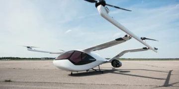 A sleek, white electric vertical takeoff and landing (eVTOL) aircraft with two large rotors is parked on an empty runway under a clear blue sky. With its futuristic design and dark-tinted windows, this marvel of aviation technology could soon be the darling of drone stocks investors. | 5StarsStocks