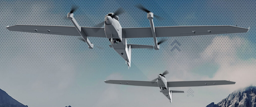 Two military drones are shown in flight against a backdrop of mountains and a cloudy sky. The drones have sleek, streamlined bodies with rotors on each wing. The image captures their front view and slightly angled right sides for a dynamic perspective, illustrating the advanced tech behind AVAV stock advancements. | 5StarsStocks