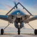 A front view of a military drone with a sleek, aerodynamic design, positioned on a runway. The sky in the background is painted with hues of orange and pink from the setting sun, creating a dramatic and picturesque scene—a testament to innovations impacting Aerospace & Defense Stocks. | 5StarsStocks