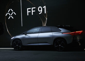Sleek silver Faraday Future FF 91 electric SUV showcased indoors with a dark background and illuminated brand logo. The vehicle is side-facing, highlighting its modern design and stylish black wheels under soft ambient lighting—an exciting prospect akin to discovering the top penny stocks to buy now for June 2024. | 5StarsStocks