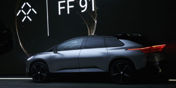 Sleek silver Faraday Future FF 91 electric SUV showcased indoors with a dark background and illuminated brand logo. The vehicle is side-facing, highlighting its modern design and stylish black wheels under soft ambient lighting—an exciting prospect akin to discovering the top penny stocks to buy now for June 2024. | 5StarsStocks
