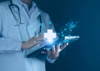 A medical professional in a white coat and stethoscope touches a glowing tablet with a holographic display of a healthcare cross and AI symbols, representing digital health technology, artificial intelligence, and the future potential of healthcare stocks. The background is dark and blurred. | 5StarsStocks