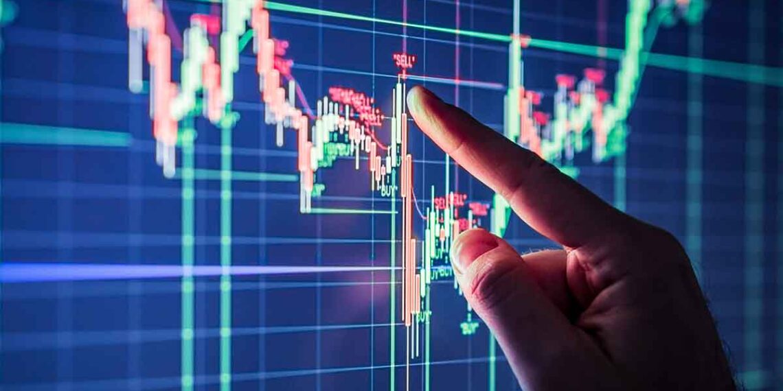 A hand points to a financial chart on a computer screen, indicating fluctuating stock market data with red and green candlestick patterns. The chart features multiple intersecting lines with price points, illustrating stocks trading trends and analysis. | 5StarsStocks