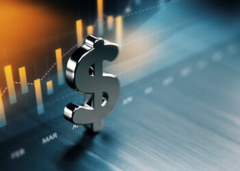A metallic dollar sign stands in the foreground with a blurred financial graph in the background. The graph shows fluctuating bar and line charts indicating market trends, particularly in dividend stocks. The colors are primarily blue and orange, signifying a dynamic financial environment. | 5StarsStocks