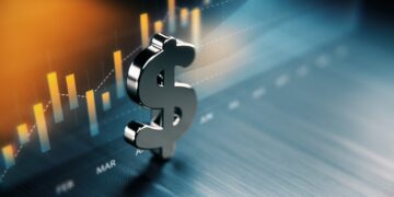 A metallic dollar sign stands in the foreground with a blurred financial graph in the background. The graph shows fluctuating bar and line charts indicating market trends, particularly in dividend stocks. The colors are primarily blue and orange, signifying a dynamic financial environment. | 5StarsStocks