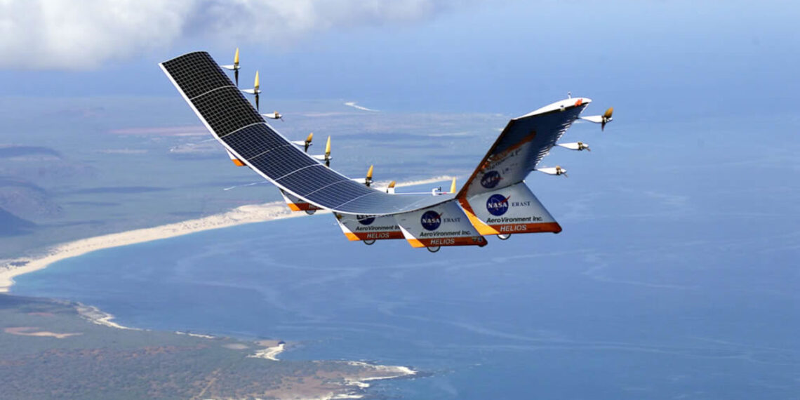A solar-powered aircraft with multiple propellers and solar panels on its wings flies over a coastal landscape. The coastline features sandy beaches and lush greenery, while blue ocean waters extend into the horizon. The aircraft, resembling innovative designs like AVAV stock, has NASA logos on its body. | 5StarsStocks