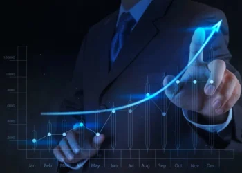 A person in a suit is pointing at a glowing, upward-trending graph that spans from January to December. The graph, resembling growth stocks, shows fluctuating data points with a noticeable rise toward the end of the year, symbolizing growth and success. | 5StarsStocks