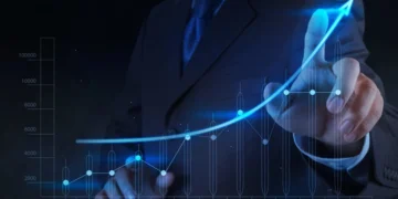 A person in a suit is pointing at a glowing, upward-trending graph that spans from January to December. The graph, resembling growth stocks, shows fluctuating data points with a noticeable rise toward the end of the year, symbolizing growth and success. | 5StarsStocks