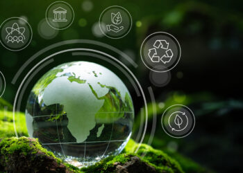 A glass globe depicting Africa rests on a bed of moss, surrounded by nature-themed icons including recycling, renewable energy, and sustainable practices, symbolizing environmental conservation and socially responsible investing in a lush, green environment. | 5StarsStocks