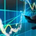 A hand points a pen at a digital screen displaying financial graphs and charts. Various colorful lines depict stock market trends, with bar graphs representing data points, including undervalued stocks. The background is dark with light blue and green neon-like hues highlighting the data. | 5StarsStocks