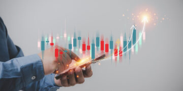 A person in a blue shirt holds a smartphone, interacting with it. Above the phone, a holographic image from 5StarsStocks displays financial charts with red and green bars, candlesticks, and arrows, indicating upward movement in a stock market or financial analysis. | 5StarsStocks
