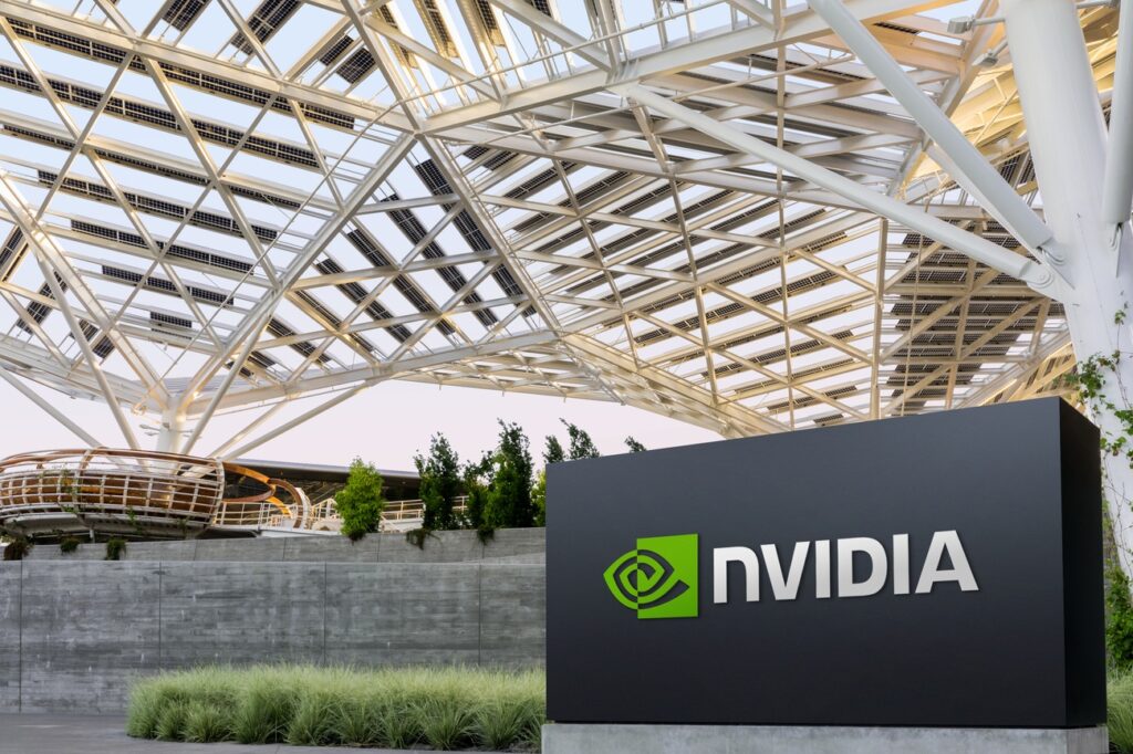 The image shows a modern architectural structure with a large Nvidia sign in the foreground. The structure features a geometric metal and glass roof with an open design. There is greenery around the base of the building, adding a touch of nature to the sleek design. | 5StarsStocks