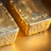 Close-up of three gold bars on a shiny surface, each marked with text. The texture and edges of the bars are clearly visible, reminiscent of the best gold stocks, with a rich golden hue reflecting the light. | 5StarsStocks
