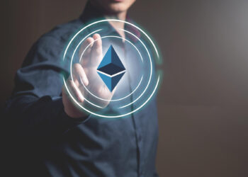 A person in a dark shirt is touching a glowing digital Ethereum logo surrounded by concentric circles, symbolizing interaction with cryptocurrency or blockchain technology. | 5StarsStocks