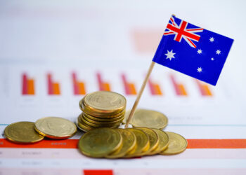 Stacks of Australian coins and a small Australian flag on a toothpick sit on financial charts with bar graphs in the background, symbolizing Australia’s economy or financial market. | 5StarsStocks