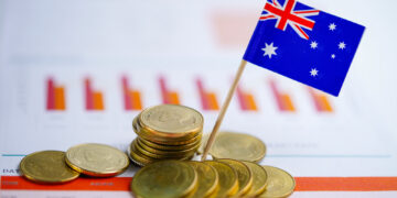 Stacks of Australian coins and a small Australian flag on a toothpick sit on financial charts with bar graphs in the background, symbolizing Australia’s economy or financial market. | 5StarsStocks