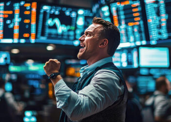 A man in business attire cheers with a clenched fist in a busy stock exchange, surrounded by large digital screens displaying financial data and stock prices. | 5StarsStocks