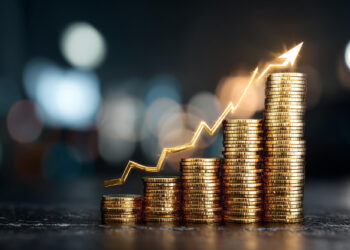 Stacks of gold coins arranged in ascending order with a glowing upward arrow graph above them, symbolizing financial growth or increasing profits. The background is blurred with bokeh lights. | 5StarsStocks