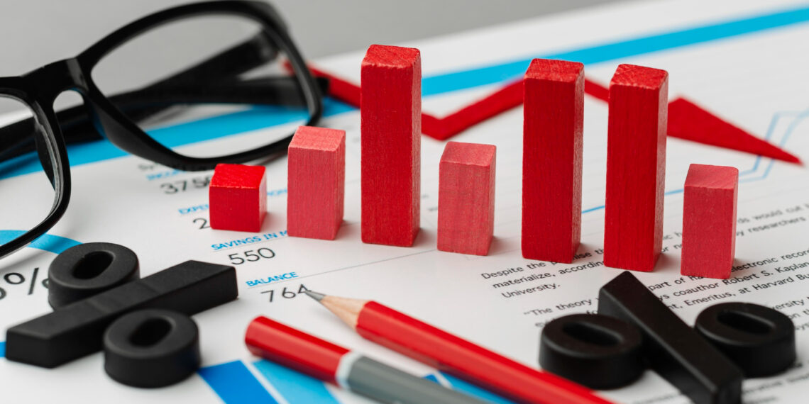 Red wooden bars, percentage symbols, pencils, and glasses are arranged on financial documents featuring charts and graphs. | 5StarsStocks