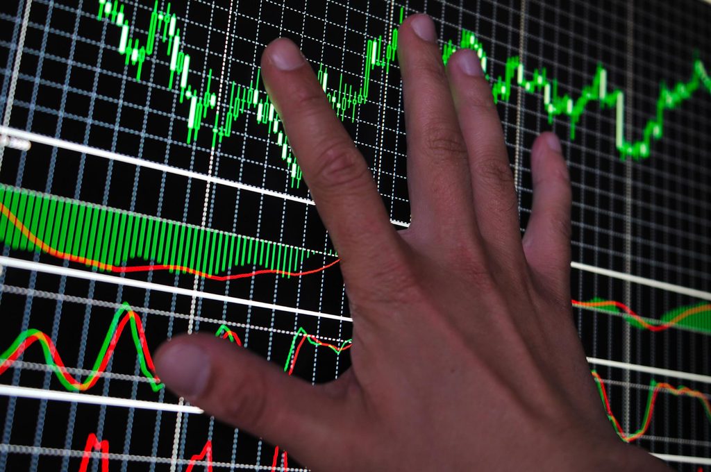 A hand reaches toward a computer screen displaying colorful financial charts and fluctuating stock market graphs on a dark background, featuring insights from 5StarsStocks.com and highlighting trends in the Cannabis sector. | 5StarsStocks
