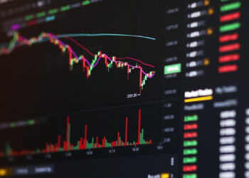 A computer screen displays a colorful cryptocurrency or stock trading chart with candlesticks, volume bars, and numerical price data, indicating market activity and price fluctuations. | 5StarsStocks