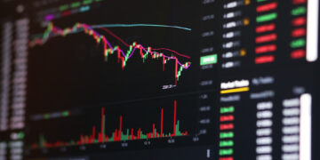 A computer screen displays a colorful cryptocurrency or stock trading chart with candlesticks, volume bars, and numerical price data, indicating market activity and price fluctuations. | 5StarsStocks