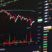 A computer screen displays a colorful cryptocurrency or stock trading chart with candlesticks, volume bars, and numerical price data, indicating market activity and price fluctuations. | 5StarsStocks