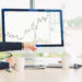 Two people in business attire sit at a desk, looking at a computer monitor displaying a rising stock chart. One person points at the screen while discussing the data. Coffee mugs and papers are on the table. | 5StarsStocks