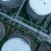 Aerial view of several large, round industrial storage tanks connected by a complex network of pipes on a grassy facility. | 5StarsStocks