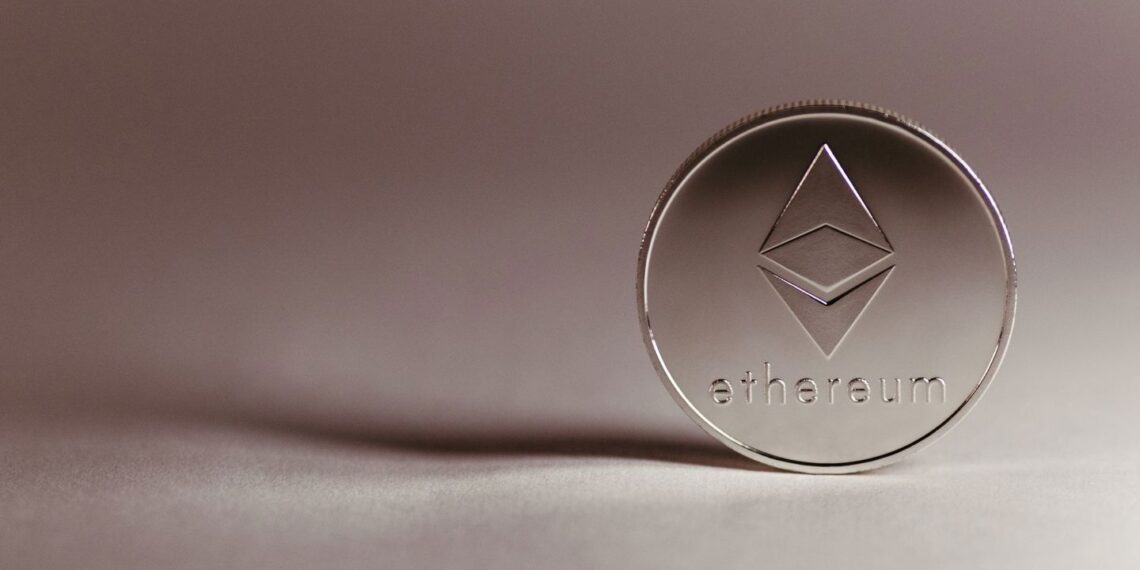 A silver Ethereum cryptocurrency coin standing upright on a neutral surface. | 5StarsStocks