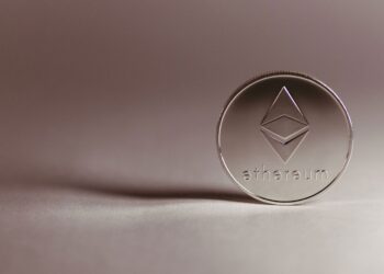 A silver Ethereum cryptocurrency coin standing upright on a neutral surface. | 5StarsStocks