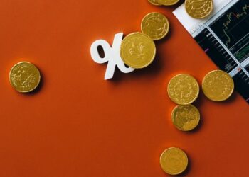 Gold coins scattered with a stock market graph and a percentage symbol on an orange background.